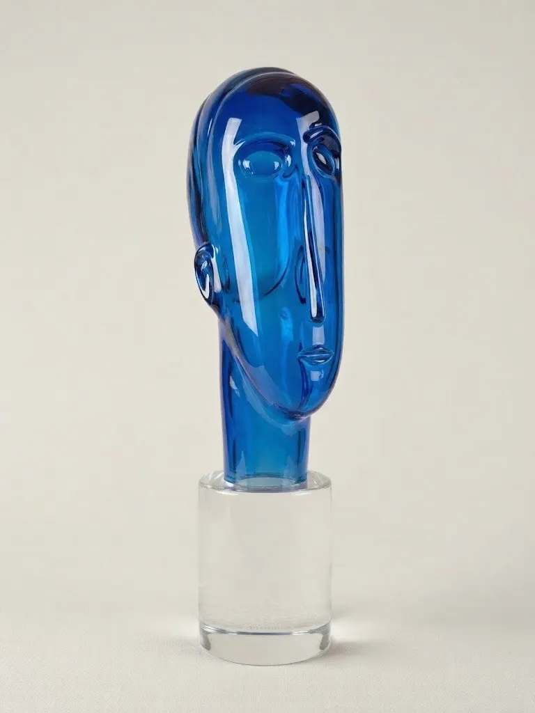 Escultura em vidro azul representando uma cabeça estilizada sobre base cilíndrica transparente
