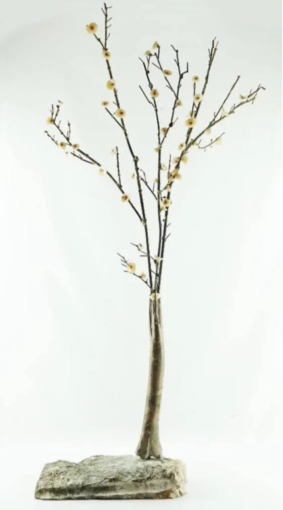 Escultura em bronze de uma árvore em flor assente numa base de pedra irregular